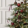 BronzeNutcracker1 Bronze nutcracker glass ornament hanging on a Christmas tree beside red baubles.