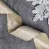 Wavy metallic Champagne Ribbon laid out on grey velvet next to frosted pine branches.