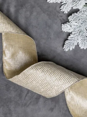 Wavy metallic Champagne Ribbon laid out on grey velvet next to frosted pine branches.