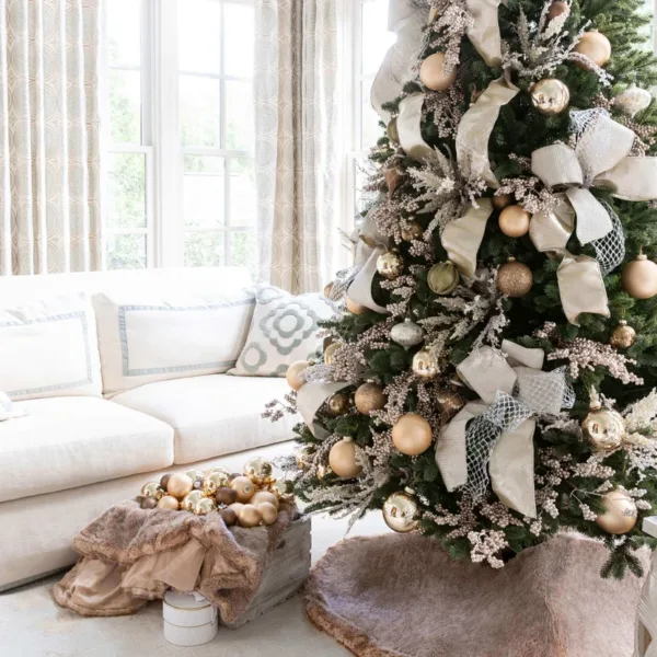 Angle view of a decorated Christmas tree with Champagne Ribbon bows and gold baubles in a bright living room.