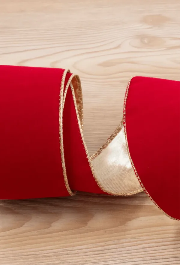 Close-up of coiled Classic Red Ribbon with metallic gold wired edging on a light wooden background.