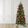 Full-length shot of a Christmas tree decorated with Classic Red Ribbon and metallic gold ornaments standing on a white tree skirt.