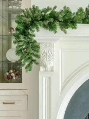 Cypress Spruce Garland with dense evergreen branches draped over the corner of an elegant white fireplace mantel.