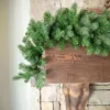 Cypress Spruce Garland featuring lush spruce foliage cascading down a dark wood beam on a stone fireplace.