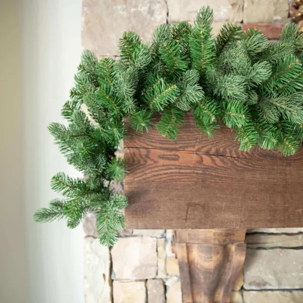 Cypress Spruce Garland featuring lush spruce foliage cascading down a dark wood beam on a stone fireplace.