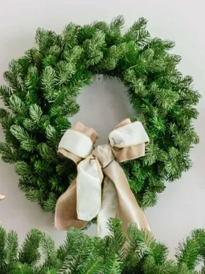 Cypress Spruce Wreath adorned with a taupe and white velvet bow hanging above a garland flanked by gold reindeer.