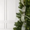 Forest Snowflake Ribbon cascading down a pre-lit Christmas tree paired with a wooden bead garland against a white wall.