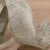 Close-up of champagne-colored Forest Snowflake Ribbon with glittery snowflake patterns coiled on a wood surface.