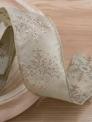 Close-up of champagne-colored Forest Snowflake Ribbon with glittery snowflake patterns coiled on a wood surface.