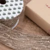 Spool of sparkling Gold Mesh Ribbon unrolled next to a wrapped gift box on a wooden surface.
