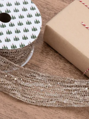 Spool of sparkling Gold Mesh Ribbon unrolled next to a wrapped gift box on a wooden surface.