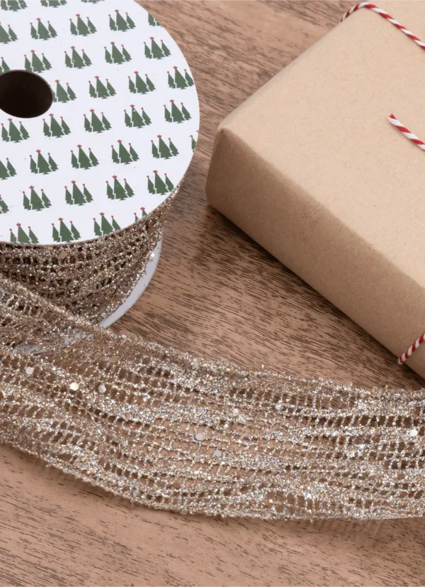 Spool of sparkling Gold Mesh Ribbon unrolled next to a wrapped gift box on a wooden surface.