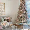 King Flock Full Artificial Christmas Tree lavishly styled with metallic rose gold ornaments and ribbon next to a grey tufted sofa.