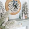 King-Flock-Wreath King Flock Wreath tied with a dusty blue velvet ribbon mounted on a woven round mirror above a light blue entry table.