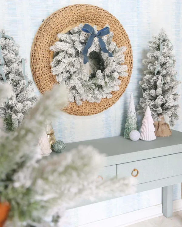 King-Flock-Wreath King Flock Wreath tied with a dusty blue velvet ribbon mounted on a woven round mirror above a light blue entry table.