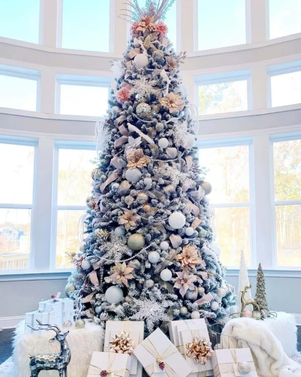 Tall King Flock Full Artificial Christmas Tree decorated with blush pink poinsettias and white ornaments in front of arched windows.