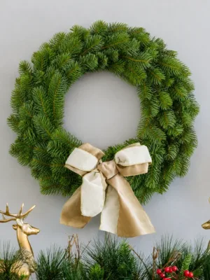 King Douglas Fir Wreath adorned with a gold and white ribbon bow hanging above a mantel flanked by gold reindeer.