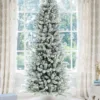 Pre-lit King Flock Slim Artificial Christmas Tree standing in front of a window at home.