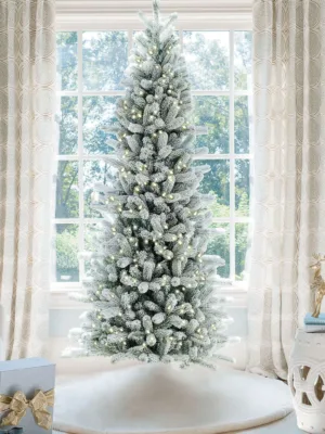 Pre-lit King Flock Slim Artificial Christmas Tree standing in front of a window at home.