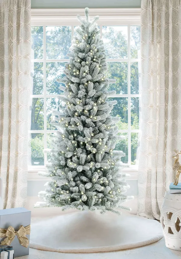 Pre-lit King Flock Slim Artificial Christmas Tree standing in front of a window at home.