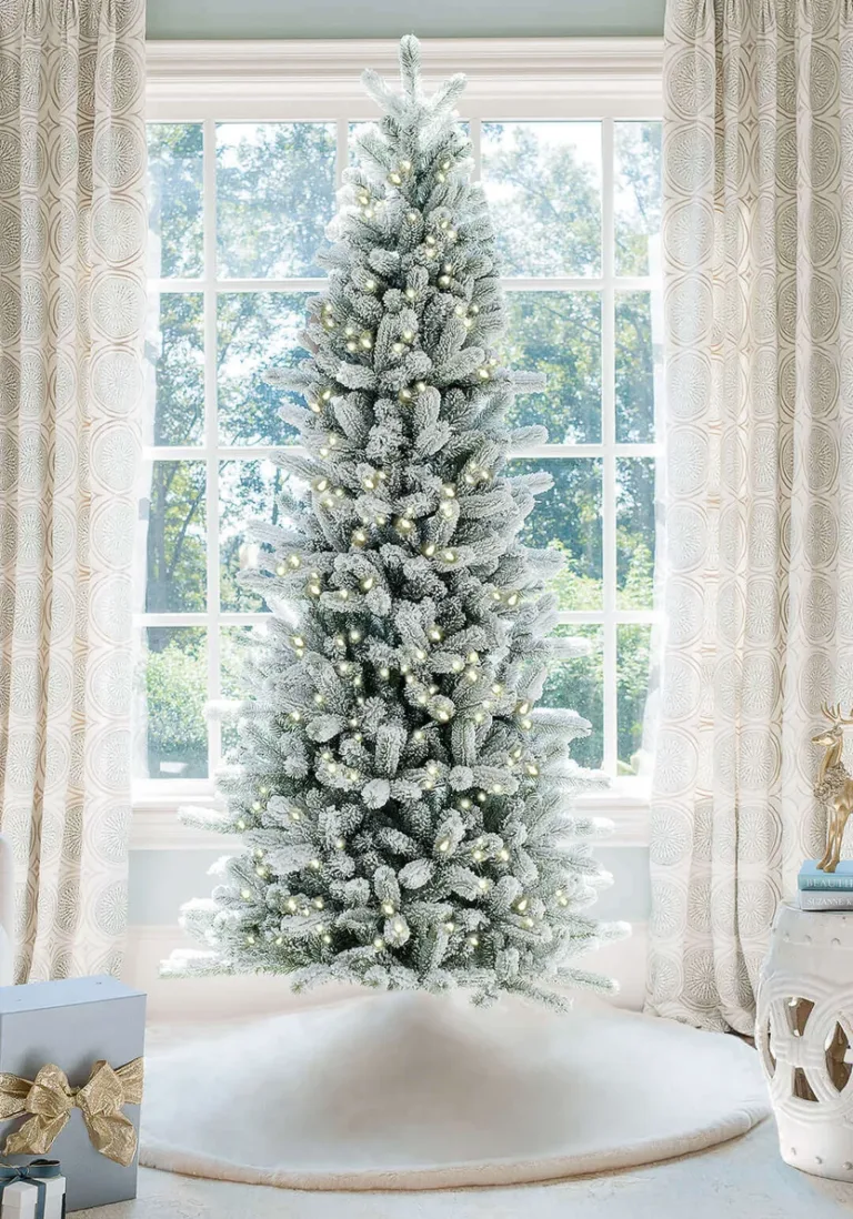 Pre-lit King Flock Slim Artificial Christmas Tree standing in front of a window at home.