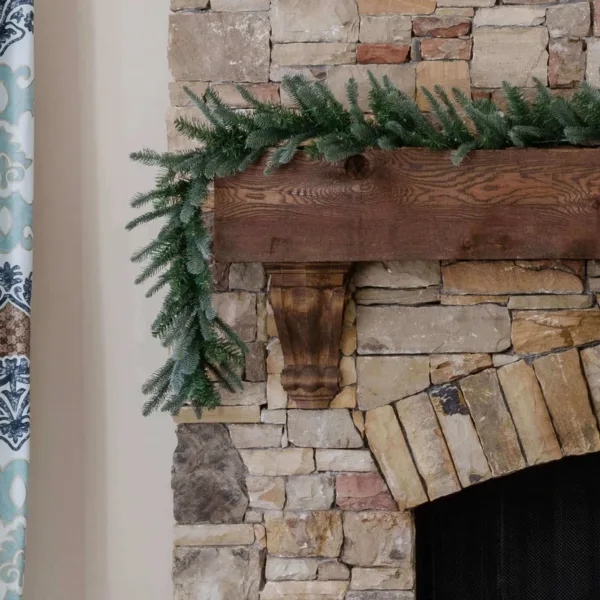 KingNobleGarland King Noble Fir Garland featuring realistic noble fir foliage cascading down a dark wood beam on a stone fireplace.