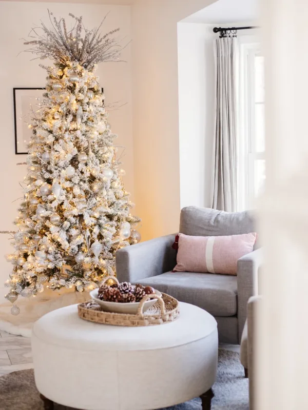Pre-lit King Flock Full Artificial Christmas Tree with silver ornaments and a starburst topper in a cozy living room nook.