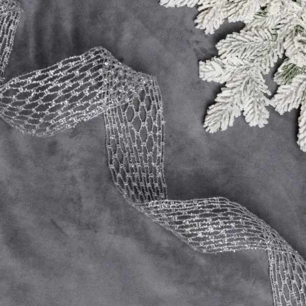 Glittery silver Netted Stretch Ribbon laid out on grey velvet next to frosted pine branches.