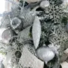 Close-up of silver Netted Stretch Ribbon draped over frosted evergreen branches with silver teardrop ornaments.