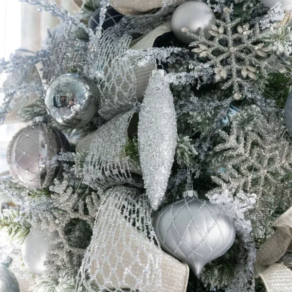 Close-up of silver Netted Stretch Ribbon draped over frosted evergreen branches with silver teardrop ornaments.