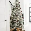 Queen Flock Slim Artificial Christmas Tree styled with black ribbons and gold baubles near a staircase with a puppy sitting below.