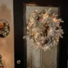 Pre-lit Queen Flock Wreath decorated with gold and copper ornaments glowing on a glass front door.