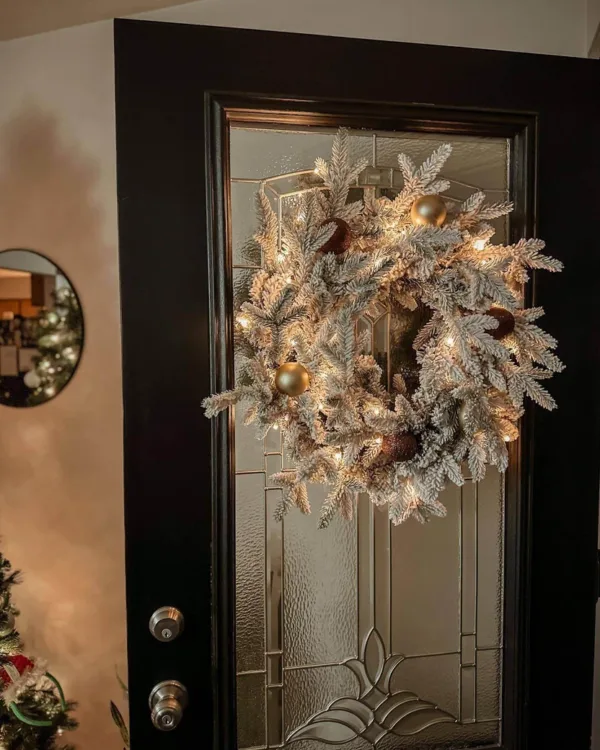 Pre-lit Queen Flock Wreath decorated with gold and copper ornaments glowing on a glass front door.