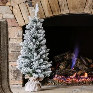 3' Queen Flock Artificial Christmas Tabletop Tree in a burlap base standing on a stone fireplace hearth next to a glowing fire.