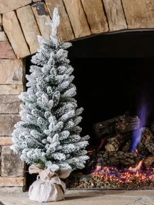 3' Queen Flock Artificial Christmas Tabletop Tree in a burlap base standing on a stone fireplace hearth next to a glowing fire.