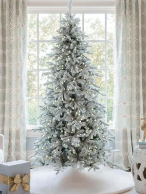 Pre-lit Queen Flock Slim Artificial Christmas Tree glowing in front of a window on a white tree skirt.