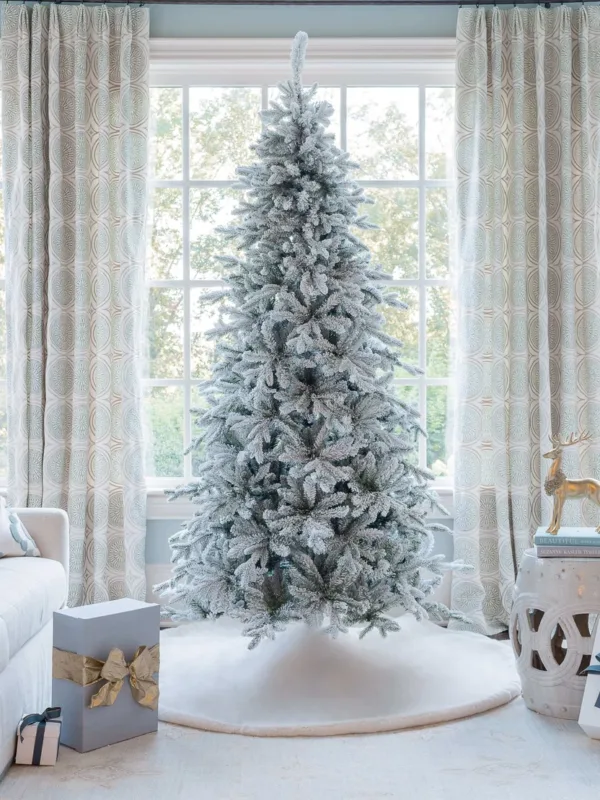 Unlit Queen Flock Slim Artificial Christmas Tree displayed in a sunlit room in front of a window.
