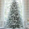 Pre-lit Queen Flock Full Artificial Christmas Tree glowing with warm lights in front of a window.