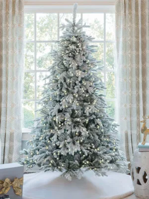 Pre-lit Queen Flock Full Artificial Christmas Tree glowing with warm lights in front of a window.