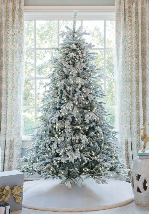 Pre-lit Queen Flock Full Artificial Christmas Tree glowing with warm lights in front of a window.