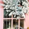 lose-up of a dense, snow-flocked Queen Flock Wreath hanging on a pastel pink front door.