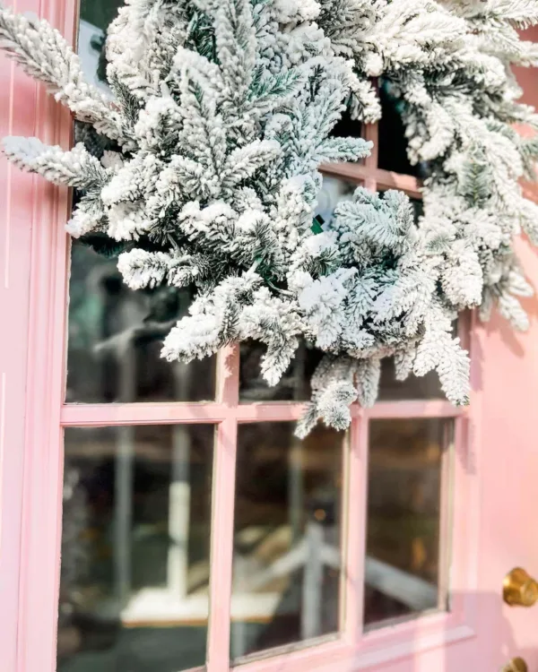 lose-up of a dense, snow-flocked Queen Flock Wreath hanging on a pastel pink front door.
