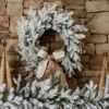Queen Flock Wreath adorned with a taupe velvet bow hanging on a stacked stone fireplace wall.