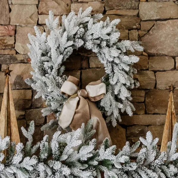 Queen Flock Wreath adorned with a taupe velvet bow hanging on a stacked stone fireplace wall.
