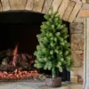 3' Royal Fir Artificial Christmas Tabletop Tree set in a rustic log base standing beside a lit stone fireplace.