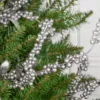 Close-up of metallic Silver Berry Picks tucked into green Christmas tree branches.