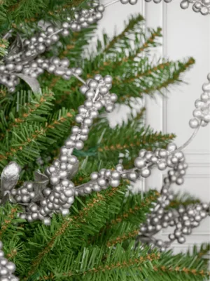 Close-up of metallic Silver Berry Picks tucked into green Christmas tree branches.