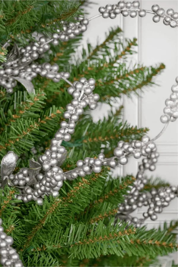 Close-up of metallic Silver Berry Picks tucked into green Christmas tree branches.