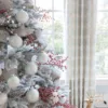 Flocked Christmas tree decorated with red Sugar Berry Picks, white ornaments, and silver ribbon.