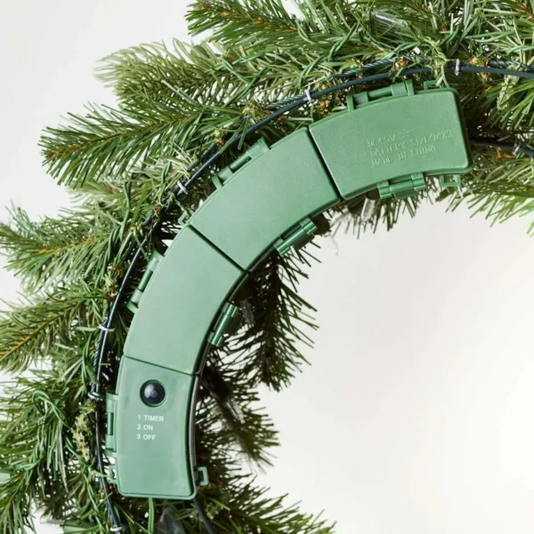 Close-up of the green battery compartment and timer control switch on the back frame of a Cypress Spruce Wreath.